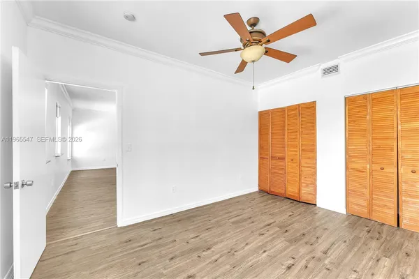 a view of an empty room with wooden floor and a ceiling fan