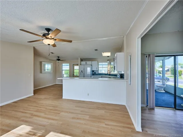 a view of an empty room and kitchen with wooden floor