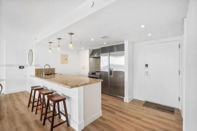 a kitchen with stainless steel appliances granite countertop a sink a stove a refrigerator and island with wooden floor