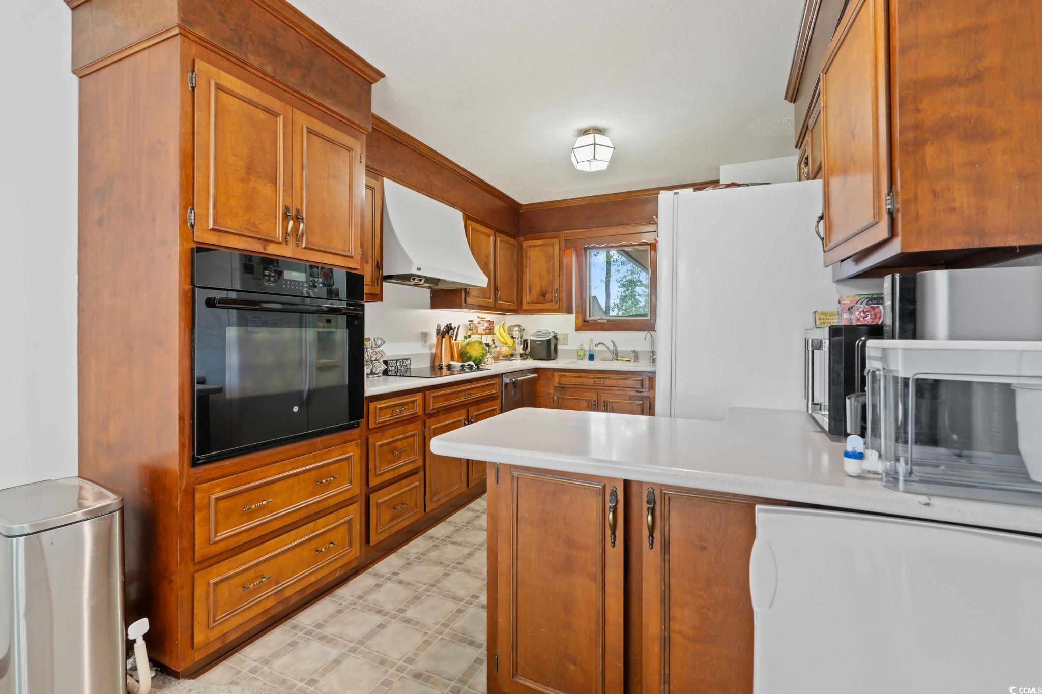 3533 Lighthouse Way Myrtle Beach, SC 29577 - Photo 14 of 40 Kitchen featuring black appliances, range hood, a peninsula, light countertops, and brown cabinets