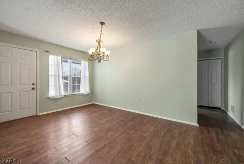 an empty room with wooden floor chandelier and windows