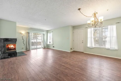 a view of an empty room with wooden floor fireplace and a window