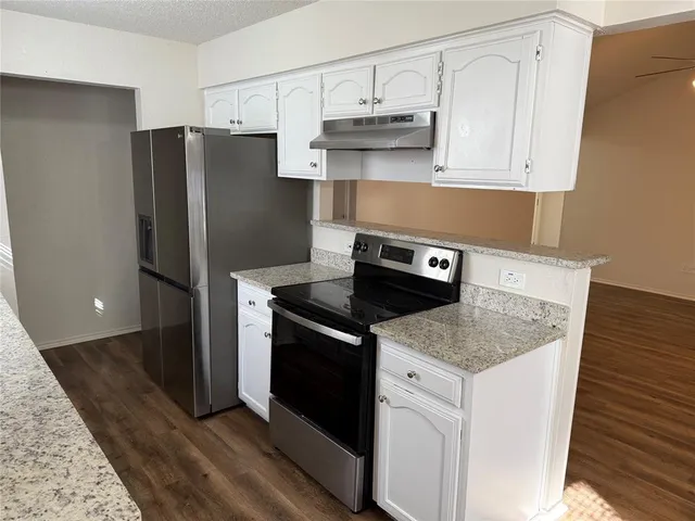 a kitchen with stainless steel appliances granite countertop a refrigerator a stove a sink and white cabinets