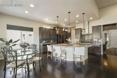 a kitchen with stainless steel appliances kitchen island granite countertop a dining table chairs and white cabinets