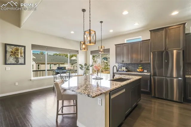 a kitchen with stainless steel appliances granite countertop a refrigerator a sink dishwasher a stove and a dining table with wooden floor