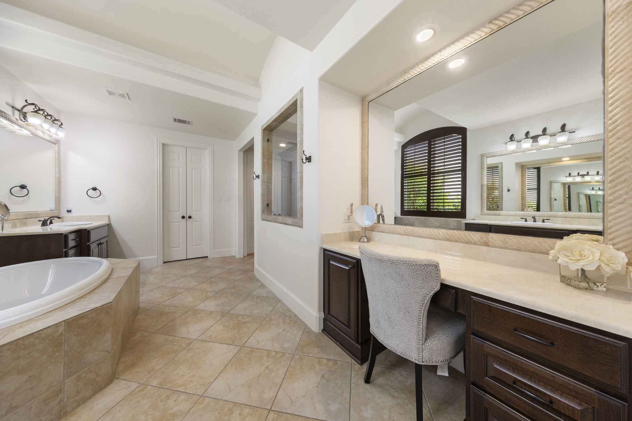 22 Marin Creek Place Spring, TX 77389 - Photo 16 of 38 Primary bath retreat featuring a soaking tub beneath shuttered windows, expansive mirrors, and a dedicated makeup vanity with custom cabinetry and refined stone finishes.