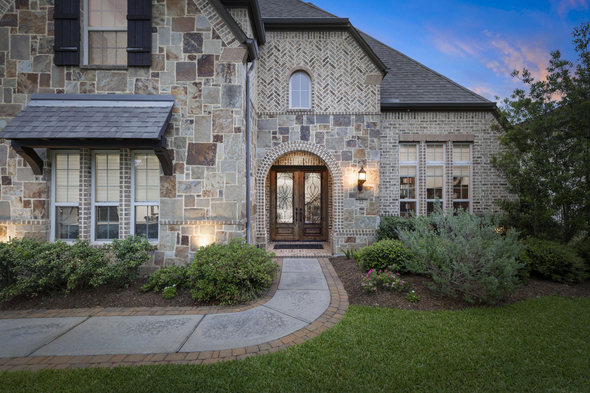 22 Marin Creek Place Spring, TX 77389 - Photo 2 of 38 Arched entry framed by rich stone and brick masonry with elegant double wood doors and decorative iron glass. Manicured landscaping and warm lighting create a welcoming arrival.