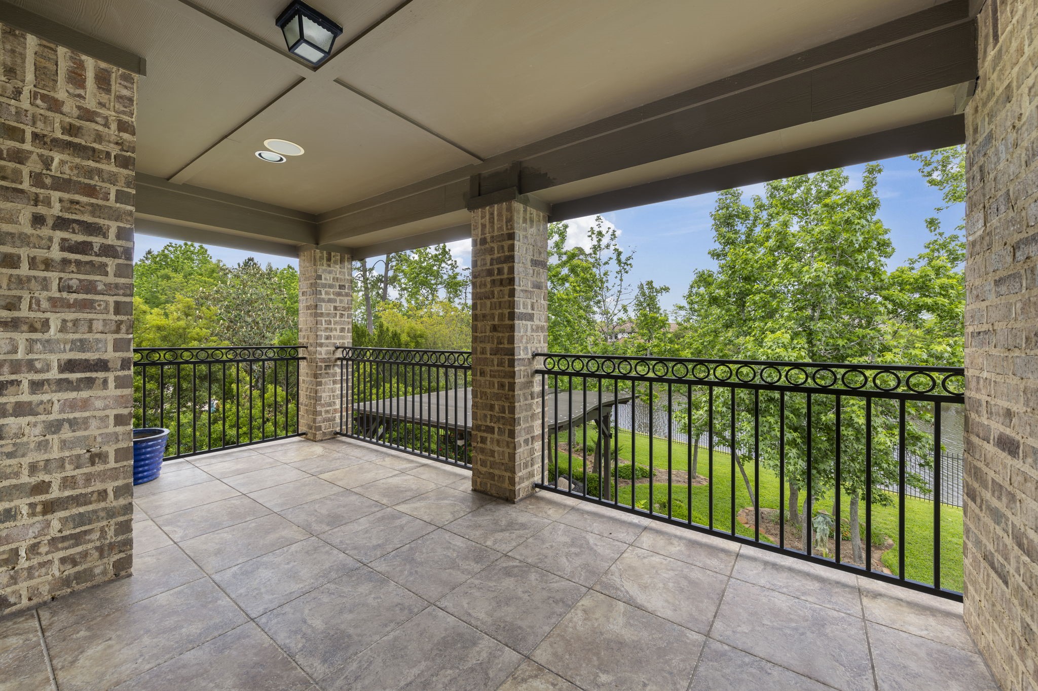 22 Marin Creek Place Spring, TX 77389 - Photo 25 of 38 Private covered balcony with brick columns and elegant iron railing, offering tranquil treetop views and a quiet setting for relaxing or enjoying morning coffee above the landscaped grounds.