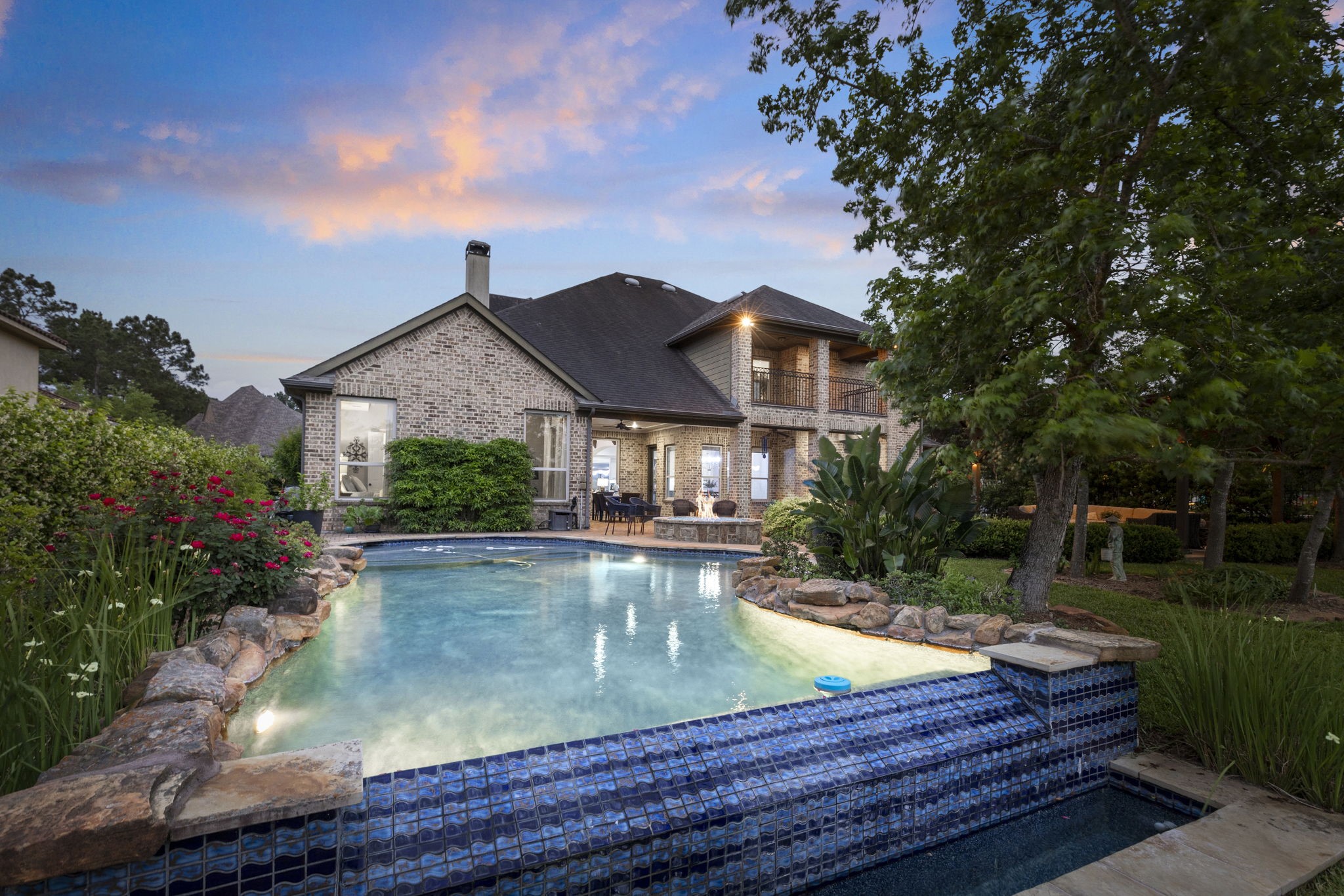 22 Marin Creek Place Spring, TX 77389 - Photo 3 of 38 Resort-style backyard featuring a freeform pool with stone accents and a tranquil waterfall edge. Covered patio and second-story balcony overlook lush landscaping, creating a private outdoor retreat.