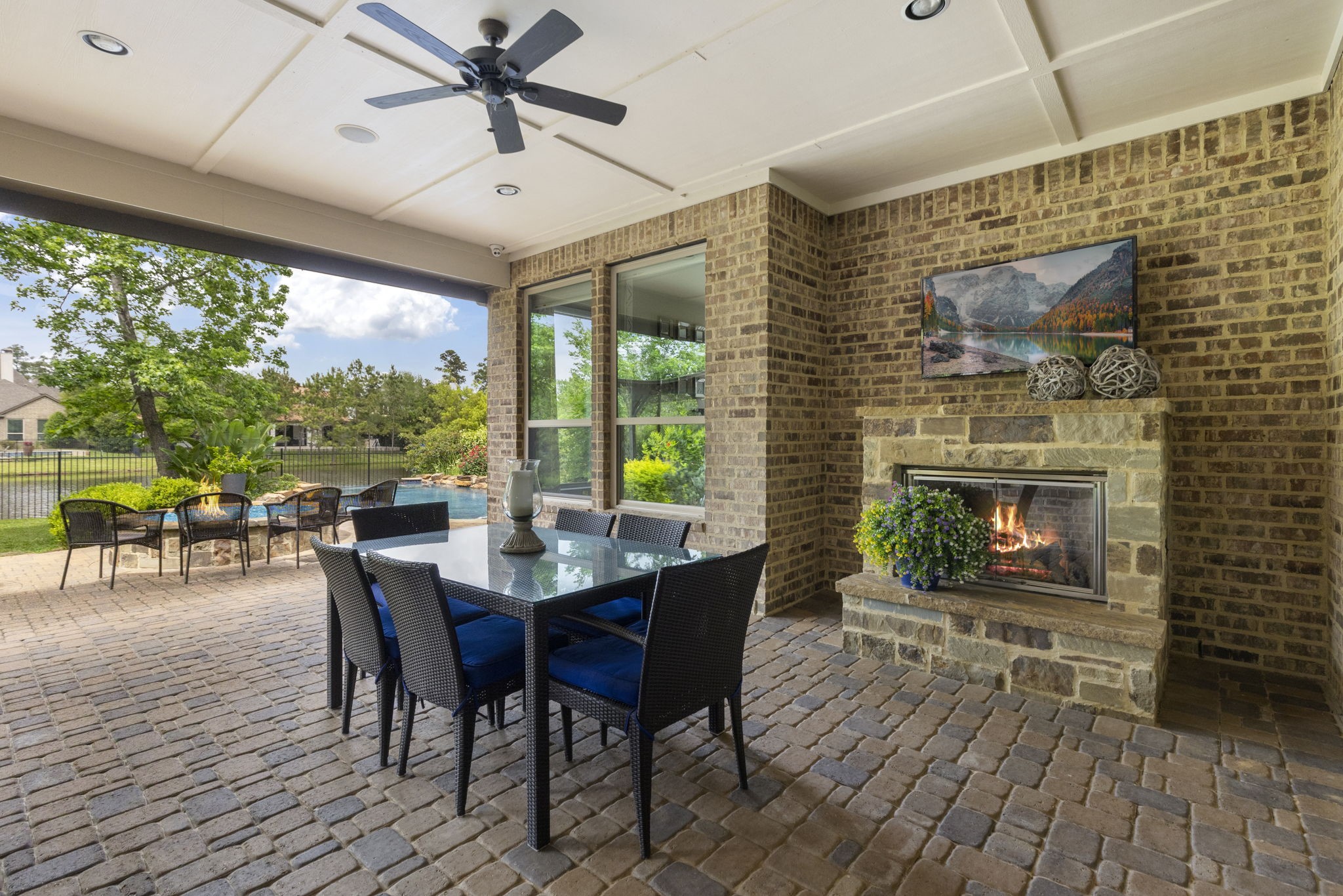 22 Marin Creek Place Spring, TX 77389 - Photo 31 of 38 Spacious covered outdoor living area with a beautiful brick fireplace and dining space, overlooking the resort-style pool and peaceful water views—ideal for entertaining and relaxing outdoors year-round.
