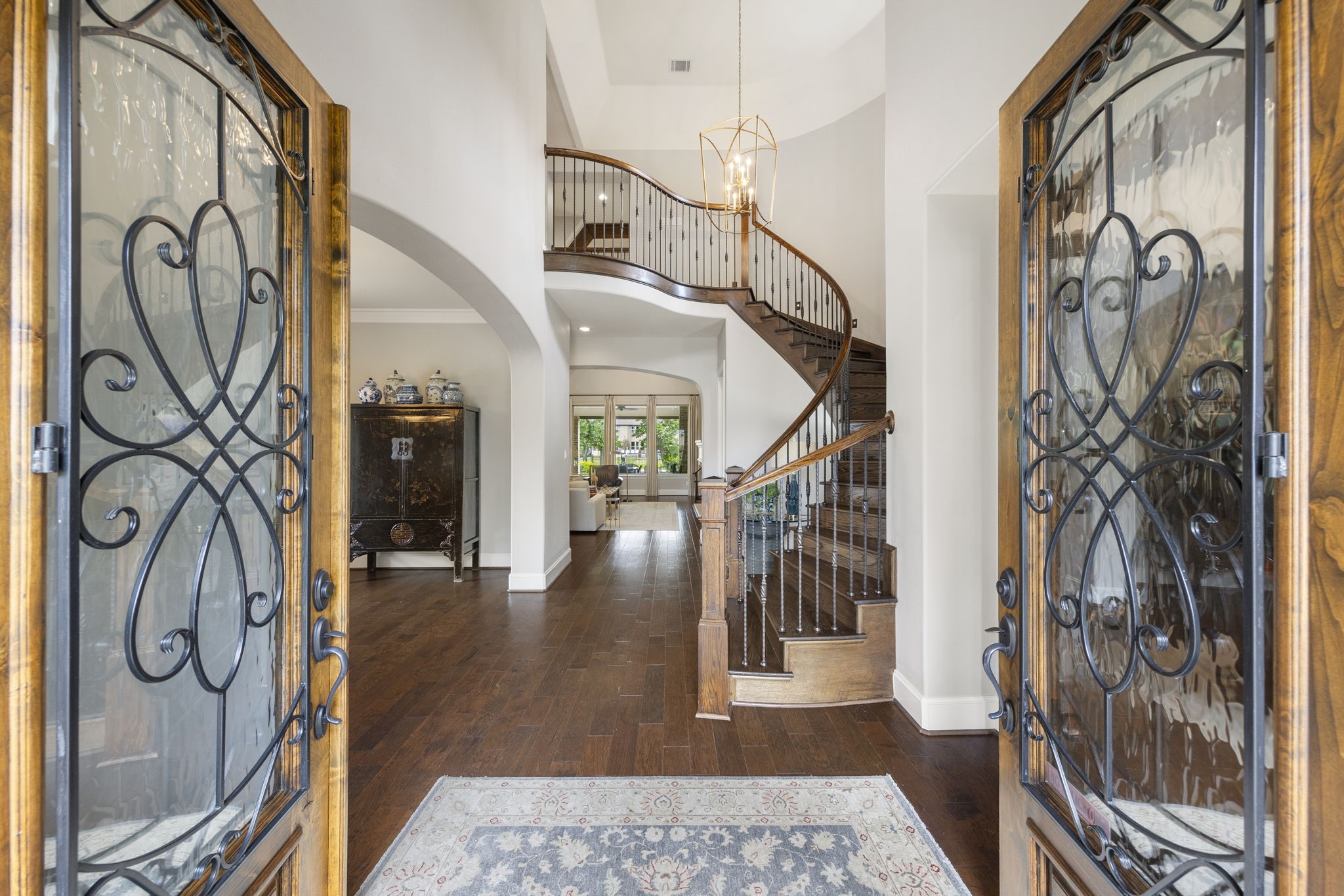 22 Marin Creek Place Spring, TX 77389 - Photo 4 of 38 Grand entry with double iron and glass doors opening to soaring ceilings, rich wood floors, and an elegant curved staircase. A stunning chandelier highlights the light-filled foyer.