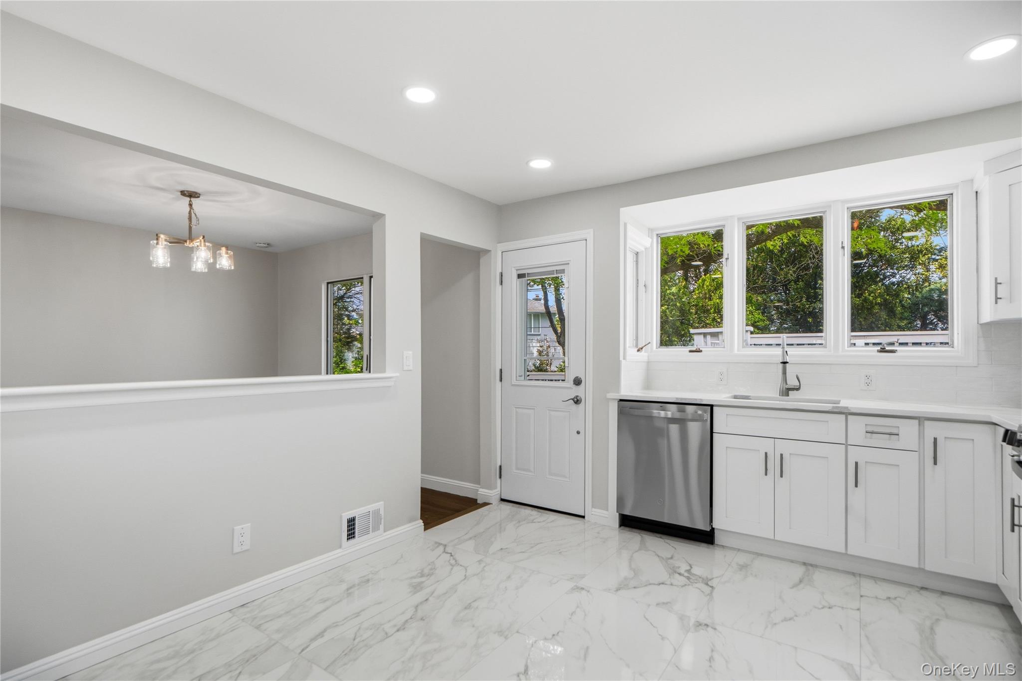 183 North Marginal Road Jericho, NY 11753 - Photo 14 of 28 Kitchen featuring white cabinetry, stainless steel dishwasher, a single basin sink, and white porcelain tile backsplash plus door to the Back Deck