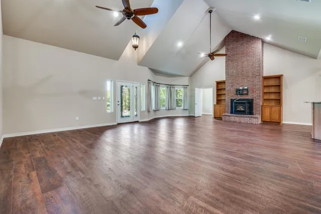 an empty room with wooden floor fireplace and windows