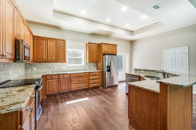 a kitchen with granite countertop a stove top oven a sink dishwasher and a refrigerator with wooden floor