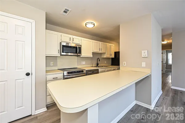 a kitchen with stainless steel appliances a stove top oven a sink a refrigerator white cabinets and wooden floor