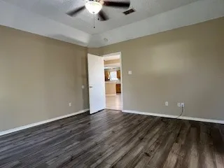 a view of an empty room with wooden floor and a ceiling fan