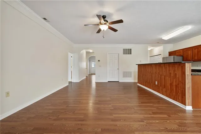 a view of an empty room with wooden floor and a ceiling fan