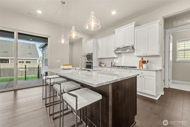 a kitchen with stainless steel appliances granite countertop a stove top oven a sink a refrigerator and white cabinets with wooden floor