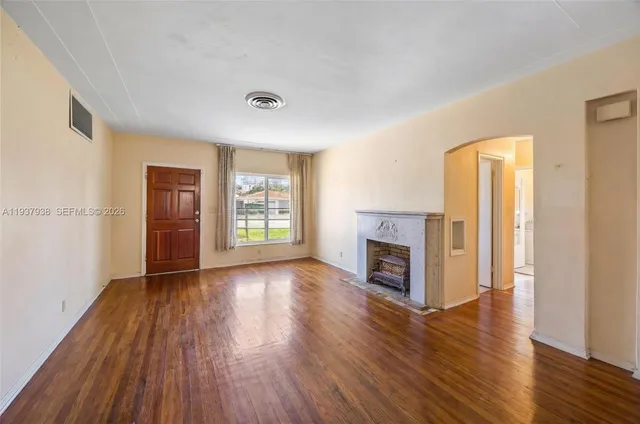 an empty room with wooden floor fireplace and windows