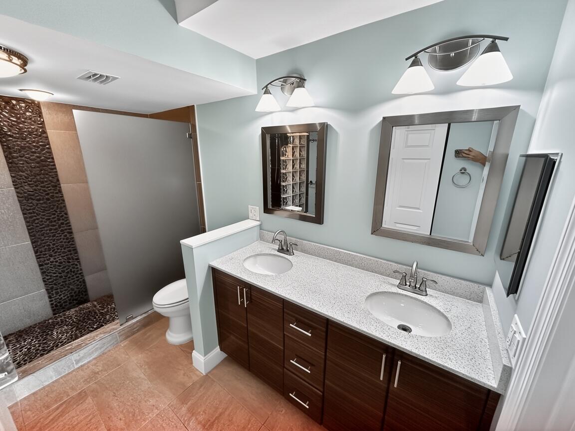 145 Atlantis Boulevard, Unit 302 Atlantis, FL 33462 - Photo 11 of 19 a bathroom with a double vanity sink a toilet and a mirror
