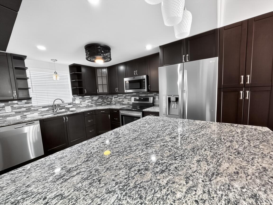 145 Atlantis Boulevard, Unit 302 Atlantis, FL 33462 - Photo 2 of 19 a kitchen with stainless steel appliances kitchen island granite countertop a refrigerator oven a sink with dishwasher and wooden cabinets
