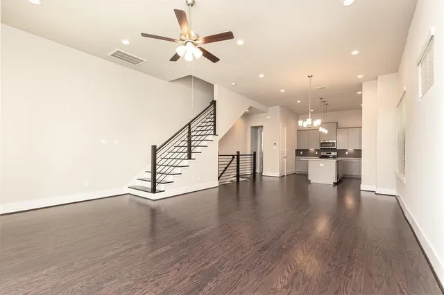 a view of an empty room with wooden floor and a ceiling fan