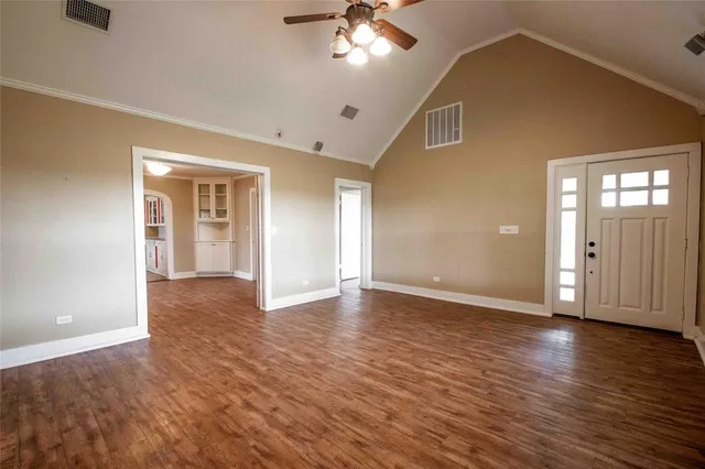 a view of an empty room with wooden floor and a ceiling fan