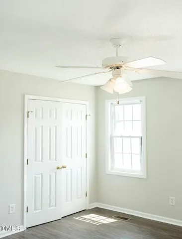 an empty room with wooden floor fan and windows