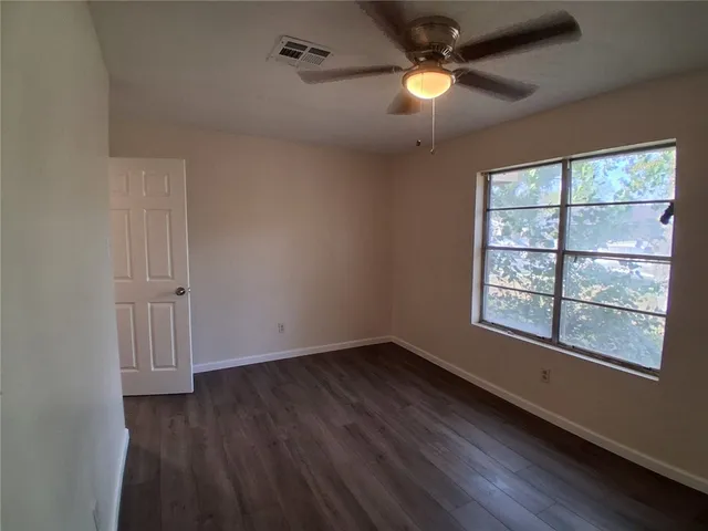 an empty room with wooden floor chandelier fan and windows