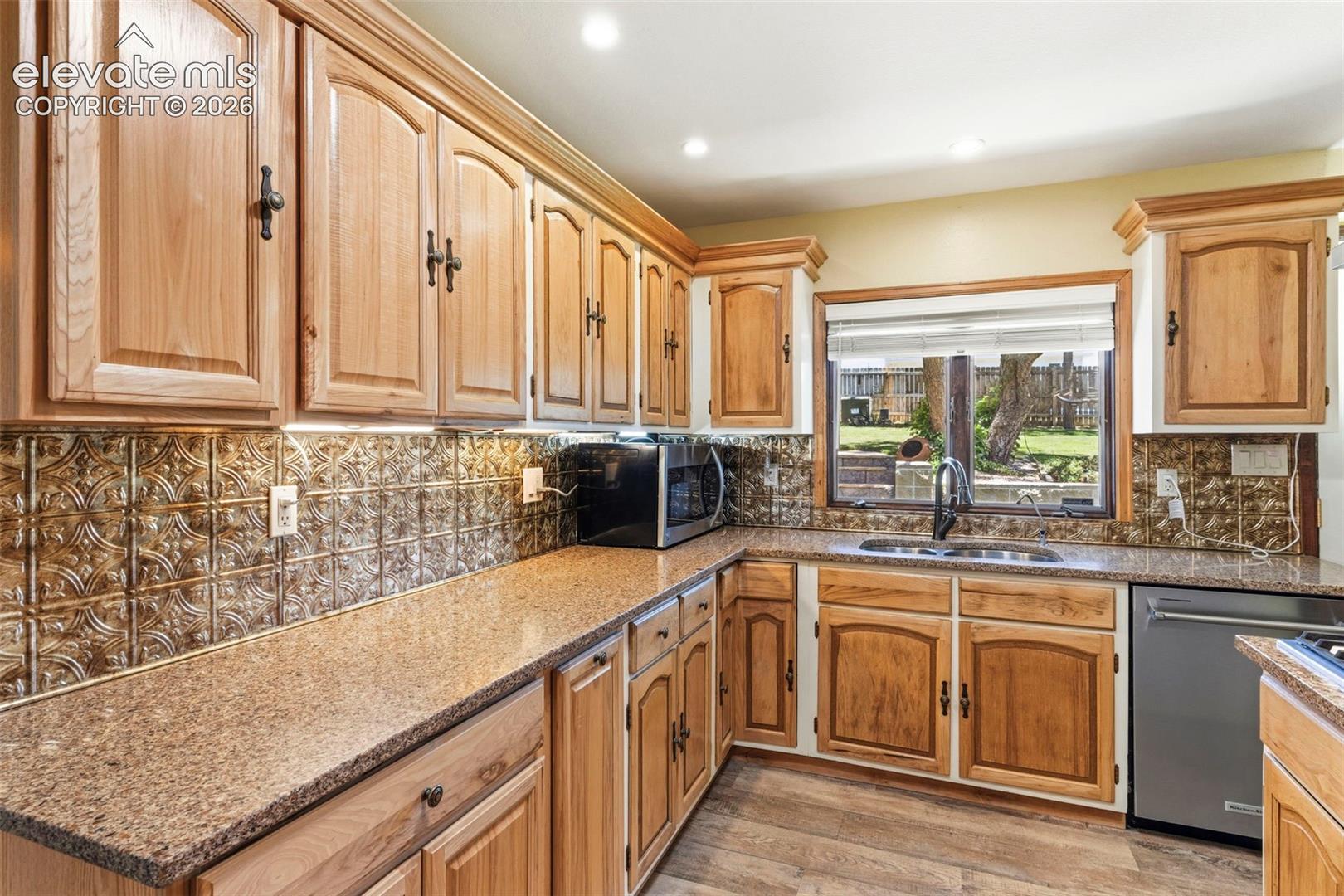 10765 Falling Star Road Fountain, CO 80817 - Photo 10 of 27 Kitchen featuring light wood cabinetry with dark hardware, speckled countertops, a textured backsplash, stainless steel appliances, and a window overlooking a green space