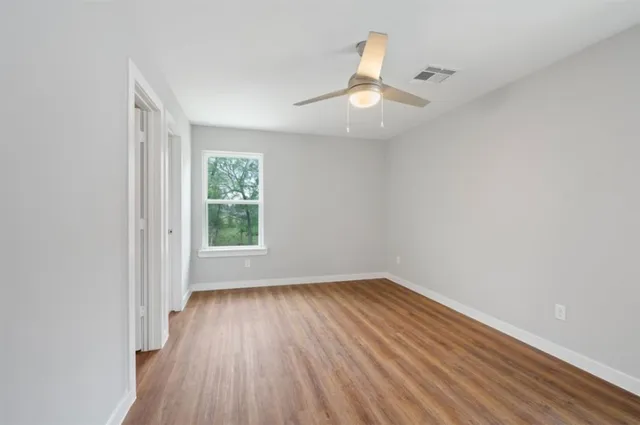 an empty room with wooden floor chandelier fan and windows