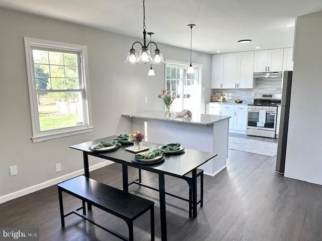 a kitchen with stainless steel appliances kitchen island a wooden table chairs and a window