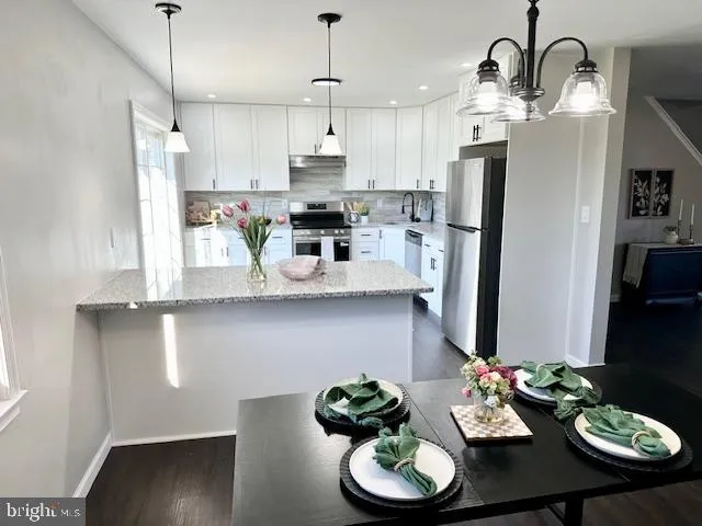 a kitchen with stainless steel appliances kitchen island granite countertop a refrigerator a stove a sink and a dining table with wooden floor