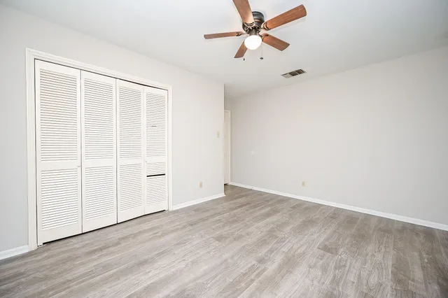 an empty room with wooden floor fan and windows