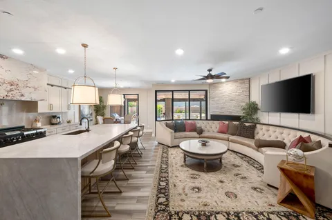 a large living room with kitchen island granite countertop furniture a rug a flat screen tv and windows