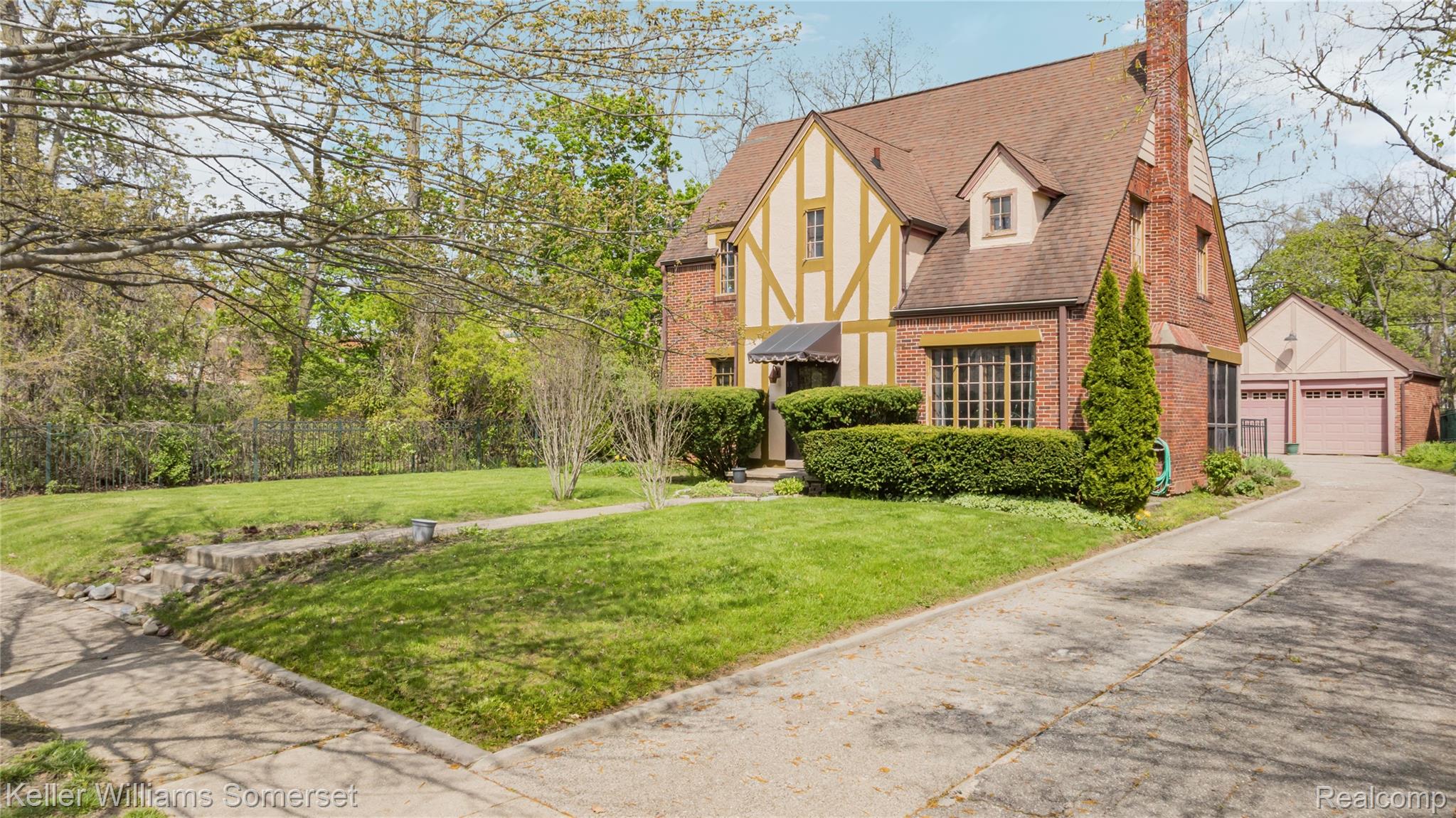 View of front of house featuring brick siding, a chimney, a garage, an outdoor structure, and a shingled roof