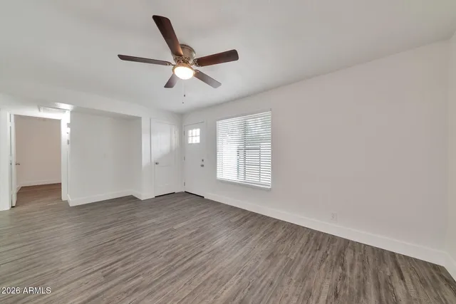 an empty room with wooden floor fan and windows