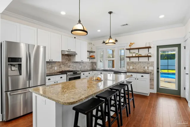 a kitchen with stainless steel appliances granite countertop a refrigerator a stove a sink a dining table and chairs with wooden floor