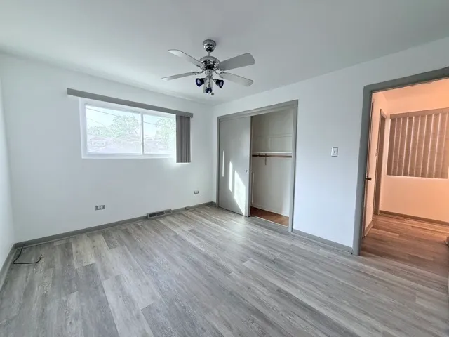 an empty room with wooden floor chandelier fan and windows