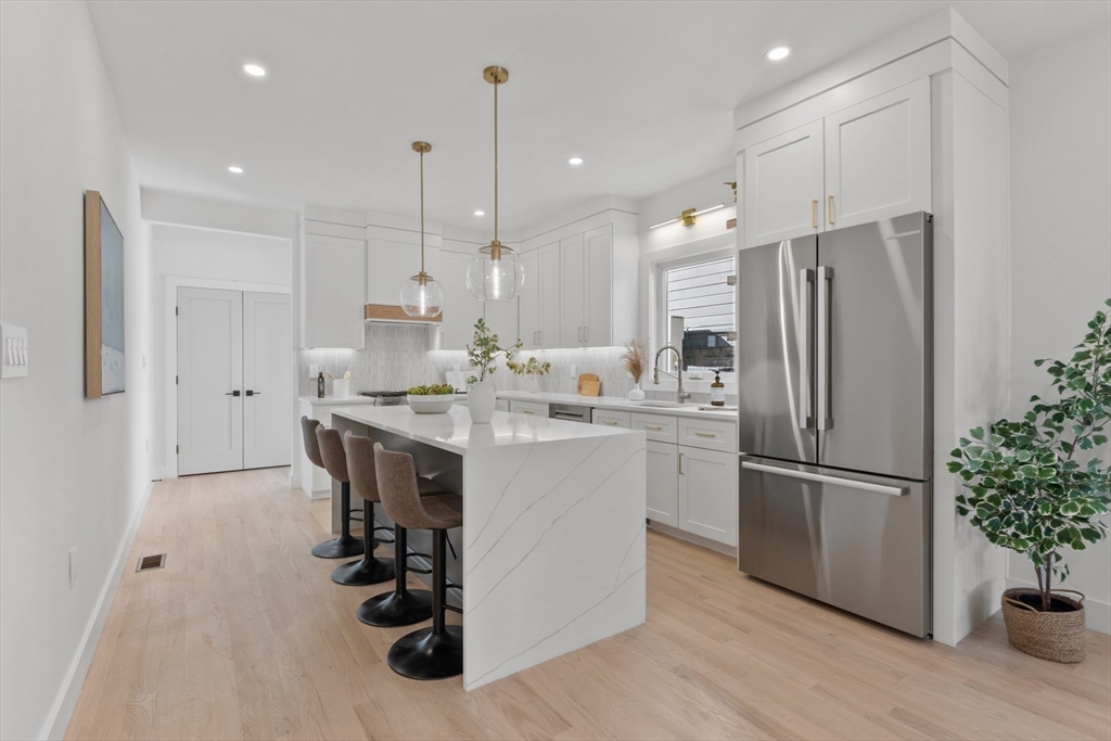 28 Sutherland Road, Unit 28 Arlington, MA 02476 - Photo 12 of 40 a kitchen with kitchen island a counter top space a refrigerator a sink and a wooden floor