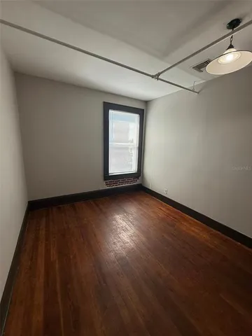 a view of an empty room with wooden floor and a window