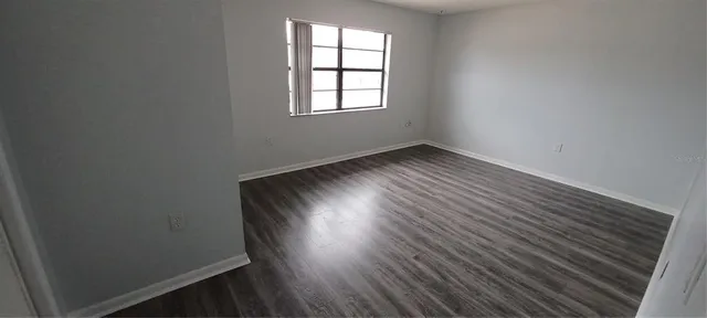 a view of an empty room with wooden floor and a window