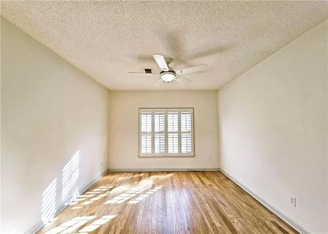 an empty room with wooden floor fan and windows
