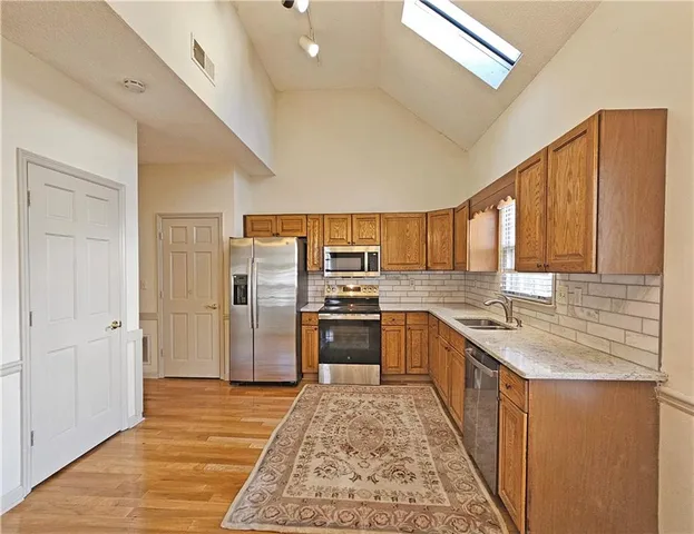 a kitchen with stainless steel appliances granite countertop a refrigerator a stove and a sink with wooden floor