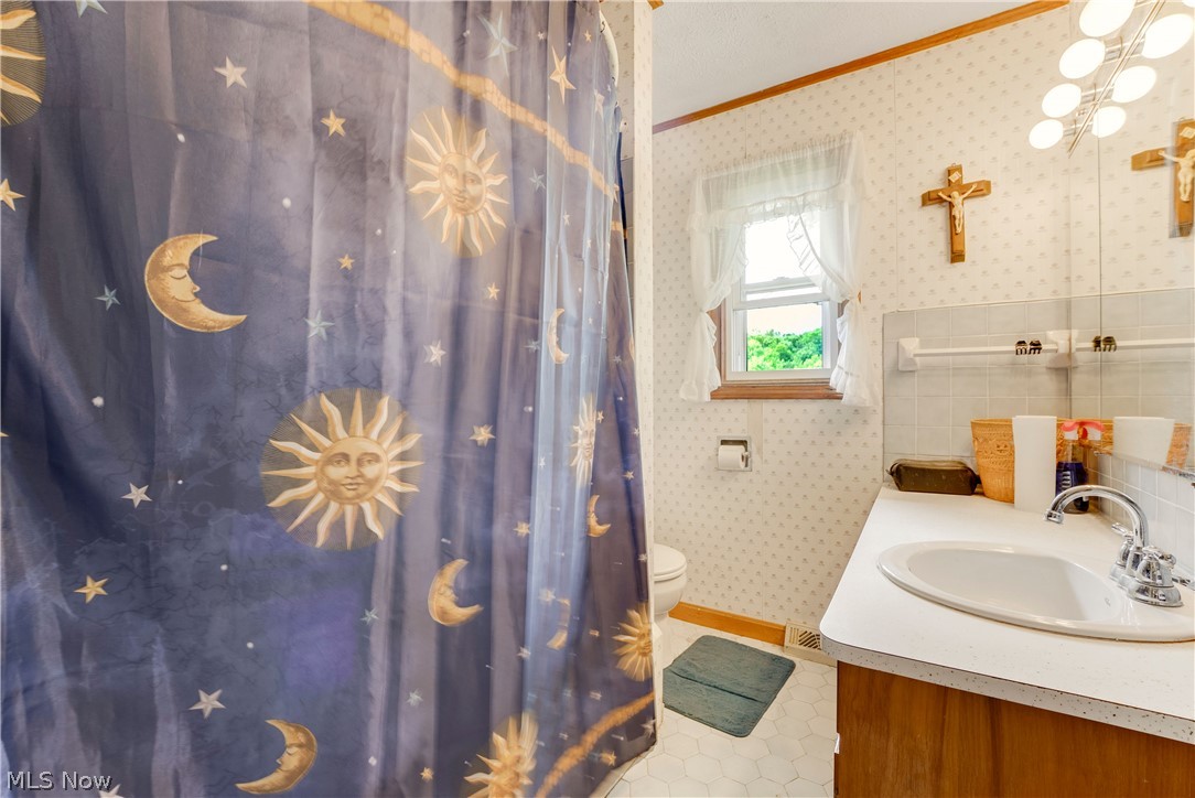 16107 Moseley Road Madison, OH 44057 - Photo 19 of 40 Bathroom featuring a window with natural light, vanity with integrated sink, wood-finish cabinetry, and patterned wallpaper