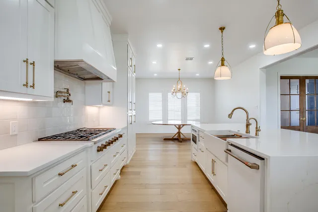 a large white kitchen with stainless steel appliances granite countertop a stove and a wooden floors