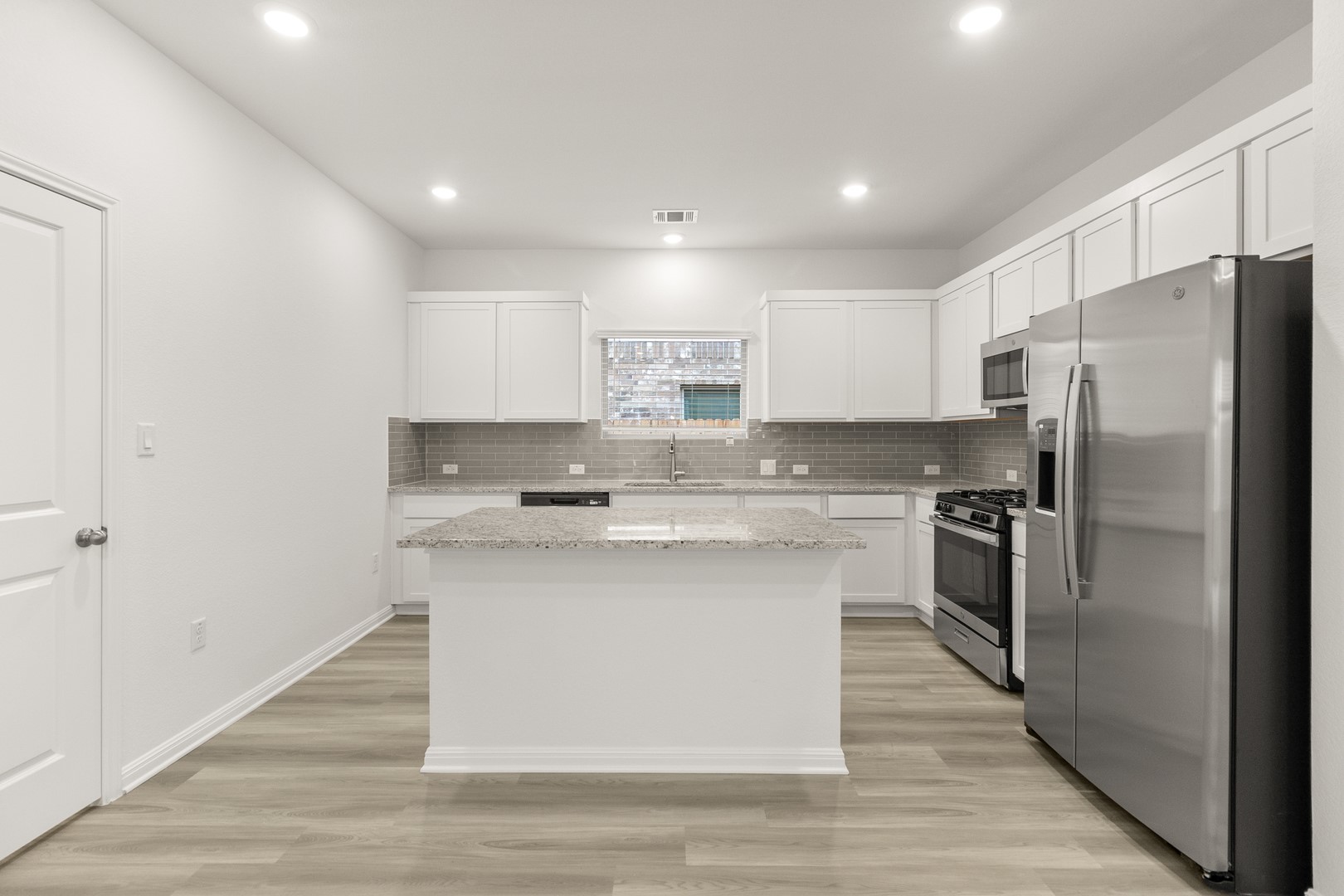 18605 Emu Lane Manor, TX 78653 - Photo 12 of 27 The kitchen features an island with a light-colored countertop, white cabinetry, and stainless steel appliances, including a refrigerator, microwave, and range