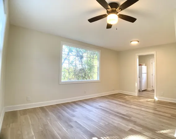 an empty room with wooden floor chandelier fan and windows