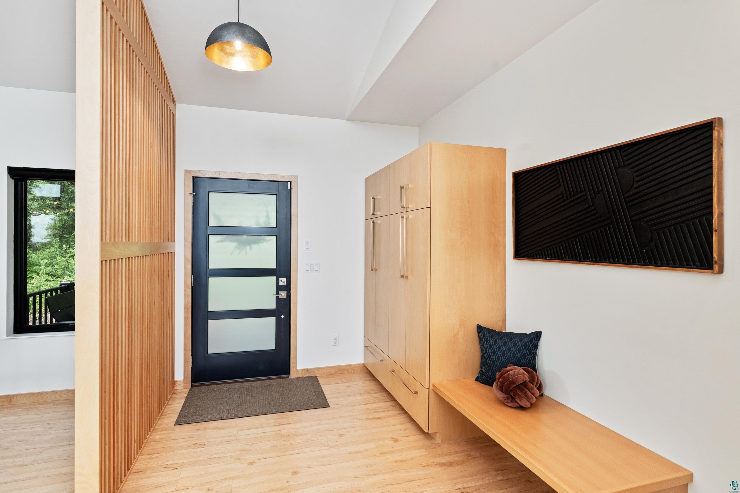 814 Pleasant View Road Duluth, MN 55803 - Photo 18 of 49 Entryway featuring wood-finish flooring, a contemporary black door with frosted glass panels, a slatted wood partition, built-in cabinetry with integrated bench seating, and a modern pendant light fixture