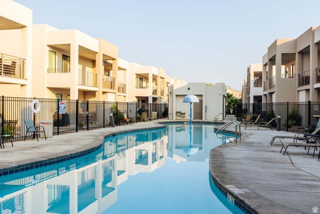 1122 South 1790th West, Unit 1 St. George, UT 84770 - Photo 32 of 37 Curved swimming pool with a concrete deck, surrounded by a black metal fence, and modern multi-story buildings featuring private balconies with metal railings